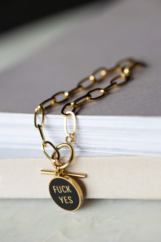 The Waterproof Gold Fuck Yes Charm Bracelet draped over the corner of a neutral surface.