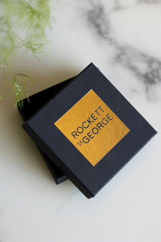 The box of the Waterproof Gold Wink Face Charm Earrings on a marble surface.