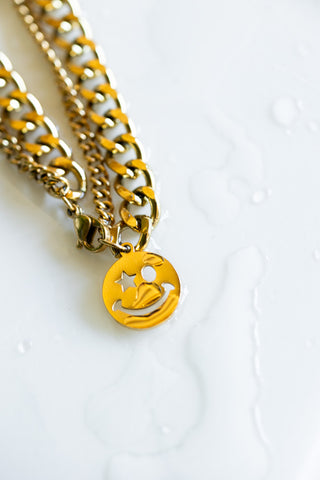 The Waterproof Wink Face Gold Chain Bracelet on a white surface with water droplets.