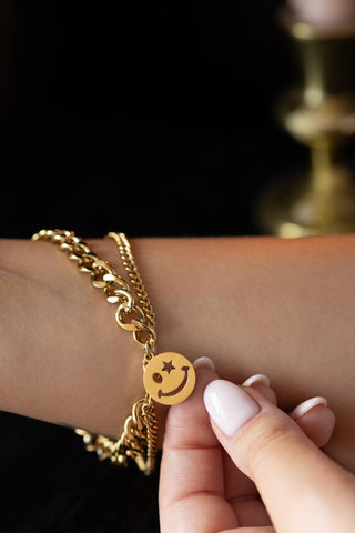 The Waterproof Wink Face Gold Chain Bracelet on a model's wrist, with the charm being held.