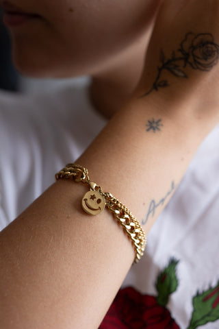 The Waterproof Wink Face Gold Chain Bracelet on a model's wrist, with their arm being held up to their face.