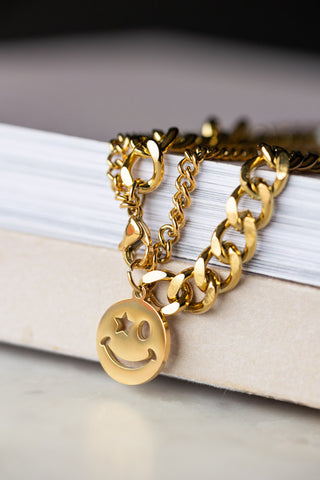 The Waterproof Wink Face Gold Chain Bracelet displayed draped across the corner of a neutral surface.