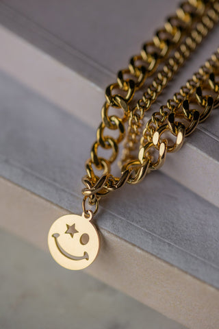 The Waterproof Wink Face Gold Duo-Chain Necklace draped across neutral surfaces.