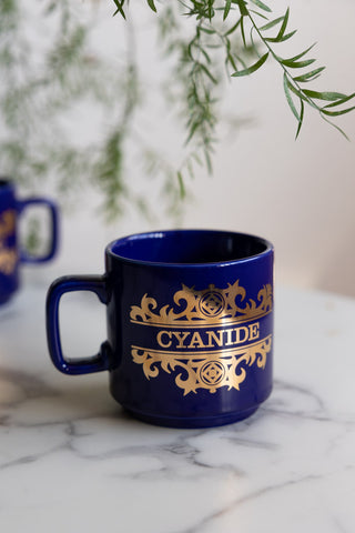 The What's Your Poison - Cyanide Mug shown on a white marble surface with a plant hanging over it.