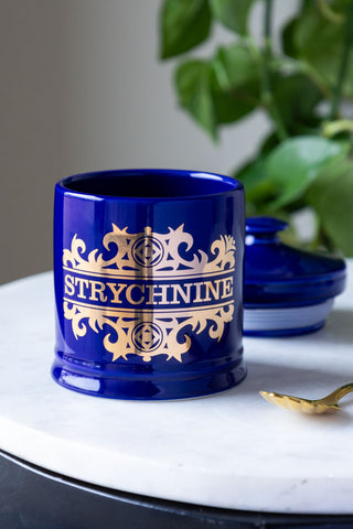 The What's Your Poison - Strychnine Jar with the lid off, styled with a gold spoon and a plant.