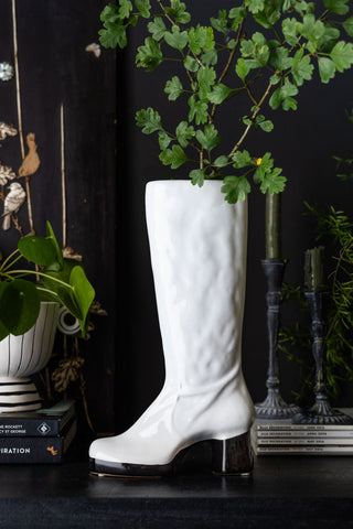 The Fabulous White Boot Vase styled on a black surface with greenery inside.