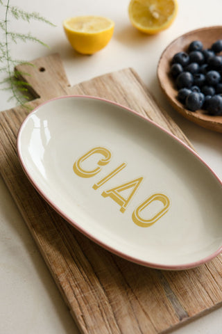 The White Ciao Plate styled on a wooden chopping board, styled with a wooden serving bowl, fruit and a plant.