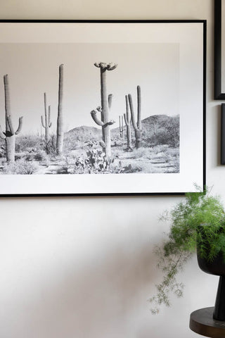 Close-up of the Wild West Cactus Art Print displayed on the wall above a side table and a plant in a pot.