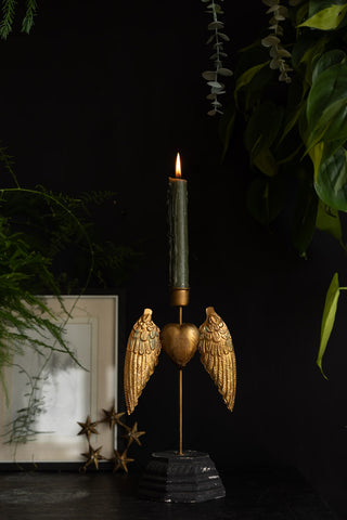 The Winged Milagro Heart Candle Holder styled with a lit candle inside, displayed on a black surface with a photo frame, star decoration and lots of greenery.