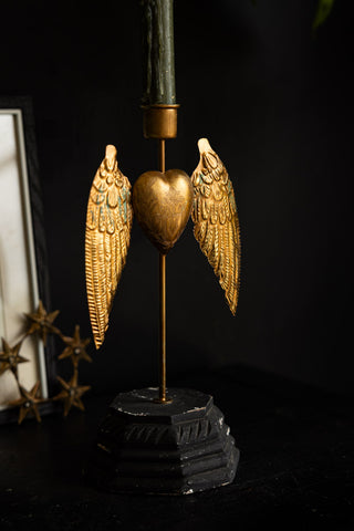 The Winged Milagro Heart Candle Holder seen from an angle, styled with a candle inside on a dark surface.