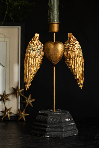 The Winged Milagro Heart Candle Holder styled with a candle inside on a dark sideboard, with home accessories in the background.