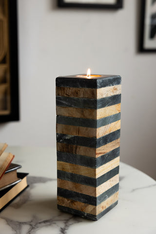 The Wood & Slate Tealight Holder on a marble table, styled with a lit tealight inside, next to some books.