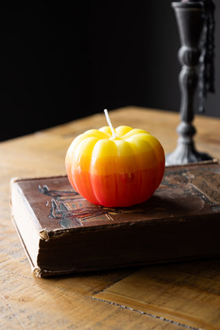 The Yellow Ombre Pumpkin Candle styled on a book, with a candlestick holder on the background.