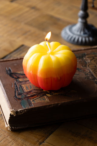 The Yellow Ombre Pumpkin Candle lit and styled on a book on a wooden surface.