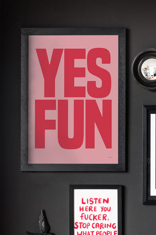 The Yes Fun Pink & Red Art Print - Unframed, displayed in a frame on a black wall with other art prints, a mirror and a wall decoration.