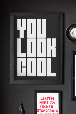 The You Look Cool Black & White Art Print - Unframed, displayed in a frame on a black wall with other art prints, a small mirror and a wall ornament.