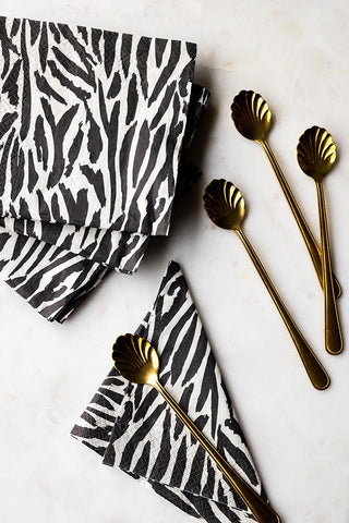 The Zebra Print Napkins - Pack Of 20 on a white surface with some gold teaspoons.