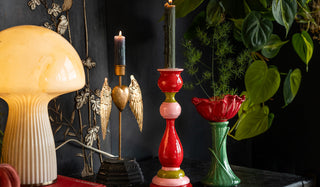 Two candlestick holders and a vase styled on a black sideboard with a book, table lamp and lots of greenery.