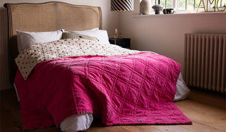 The Reversible Hot Pink Star Throw styled on a bed with a rattan headboard in a bedroom.