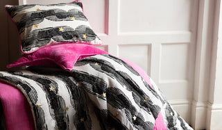 Two cushions styled on stop of a matching quilt, in front of a white wall.