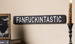 The Fanfuckintastic Sign on a wall next to a lit candle and some home accessories.