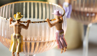 Two cowboy drinks markers displayed on the edge of a champagne coupe. 