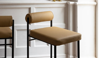 Two sand-coloured bar stools styled together in front of a white panelled wall.