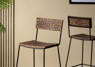 Two of the Natural Leopard Love Bar Stools displayed in front of a neutral wall, styled with a plant.