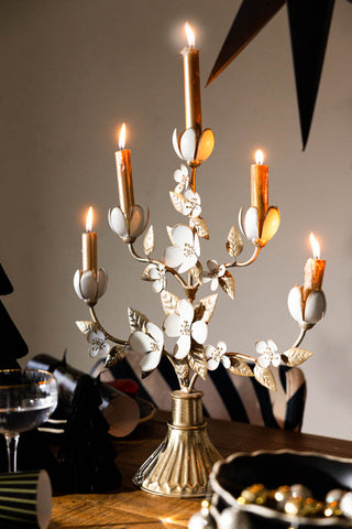 Beautiful floral candleabra with five gold candles lit on a dining table that is set for Christmas.