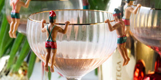 A champagne glass with elf drinks charms hanging onto the edge of the glasses.