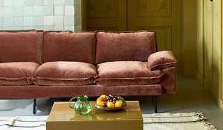 A velvet sofa styled in a living room with a rug, coffee table, glass jug and fruit bowl.