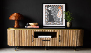 The Ribbed TV Unit styled in front of a black wall with various home accessories and a plant.