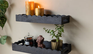 Two Black Wooden Scalloped Shelves on a  neutral wall styled with plants and candles.