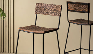 Two of the Natural Leopard Love Bar Stools in front of a neutral wall with a plant in the background.