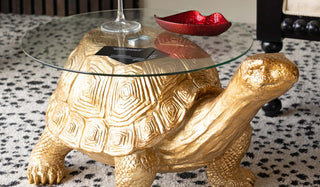 The Gold Tortoise Side Table on a rug, styled with some accessories on the glass.