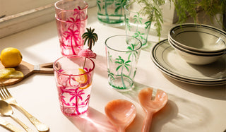 Various picnic/tableware displayed together with some fruit and greenery in the sunshine.