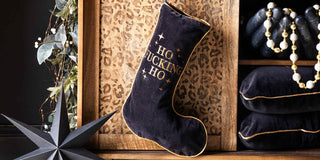 A black velvet stocking with 'ho fucking ho' embroidered on the front. The stocking is hanging from a leopard tv unit.