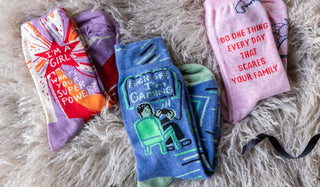 Three pairs of colourful slogan socks styled on a fluffy background.