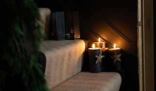 Three lit pillar candles with star candle pins in, displayed on some stairs, with a star lantern with a tealight in on the step above.