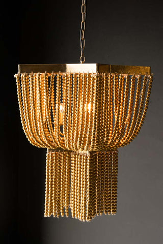 The Gold Star Shaped Beaded Statement Chandelier Light switched on, hanging in front of a black wall.