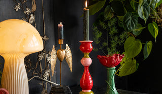 A mushroom lamp, two candlestick holders and a red flower vase, styled together on a black sideboard with some greenery.