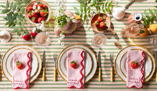 Aerial view of a summer tablescape on a stripe tablecloth, styled with various colourful tableware accessories, fruit and plants.