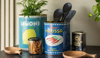 The Set Of 2 Lemon & Harissa Storage Tins - Large & Medium styled with various kitchen items and plants, on a black sidebaord.