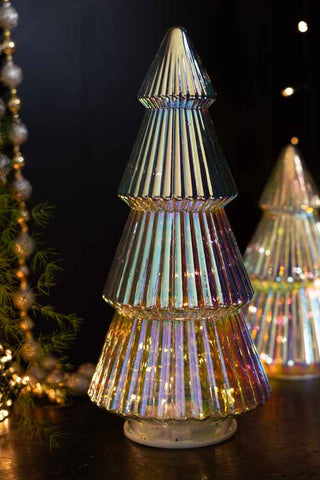 The Large Glass Christmas Tree With LED Lights styled with a smaller version in the background, next to some greenery, beads and fairy lights.