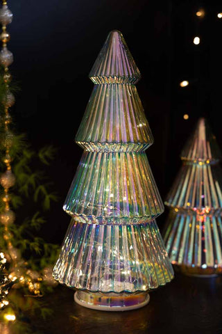 The Large Glass Christmas Tree With LED Lights with the lights switched on, displayed with a smaller version, some greenery, Christmas decorations and fairy lights.