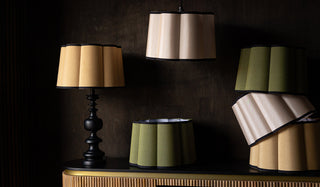 Various scalloped lampshades in different colours arrange together with a wooden sideboard, with one shade styled on a lamp base and one hanging as a pendant light.