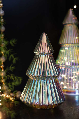 The Medium Glass Christmas Tree With LED Lights styled with the larger version in the background, displayed next to some beads, greenery and fairy lights.