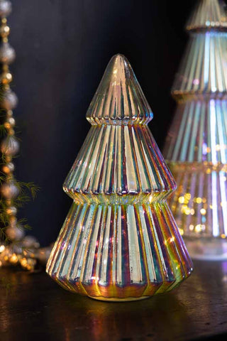 The Medium Glass Christmas Tree With LED Lights styled with the large version in the background, with some beads, greenery and fairy lights to the side of the shot.