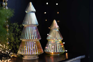 Two iridescent Christmas Tree Decorations in glass. In the background there are lit fairy lights which reflect off the iridescent trees creating a twinkling and magical festive feel.