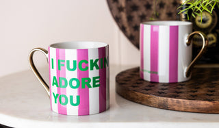 Two of the I Fucking Adore You Stripe Mugs styled together with wooden serving boards and a plant.